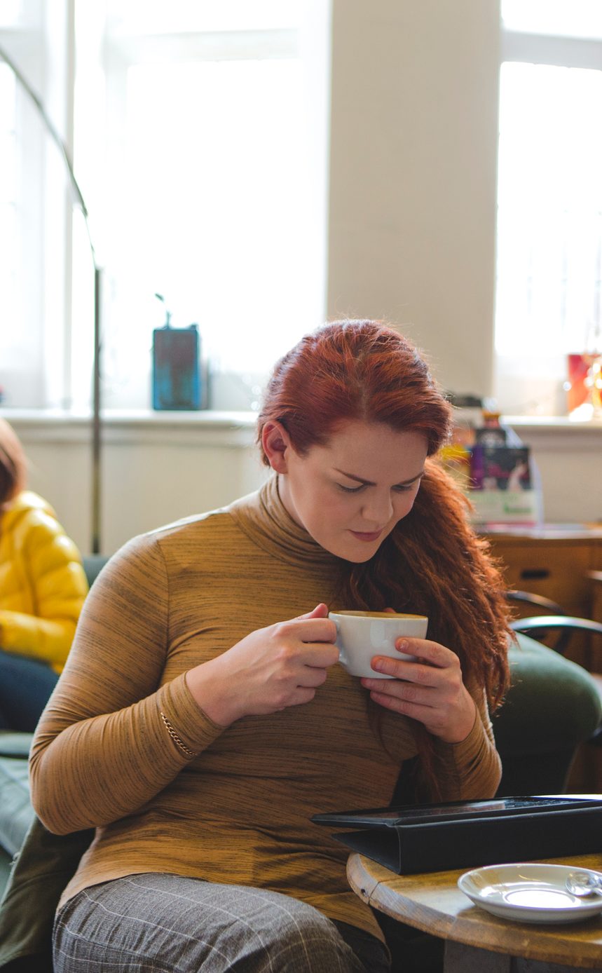 Transgender woman sitting contently with a coffee and looking at her digital tablet