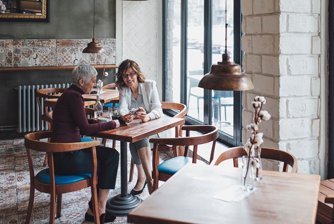 Two pretty middle-aged women sitting at coffee shop and using cell phone.